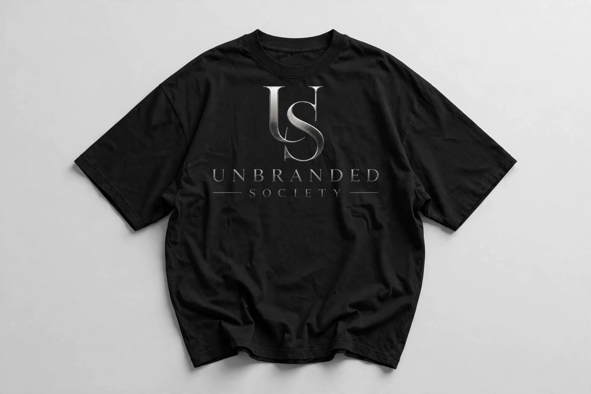 Black oversized T-shirt, front view, with the silver Unbranded Society logo on the chest.